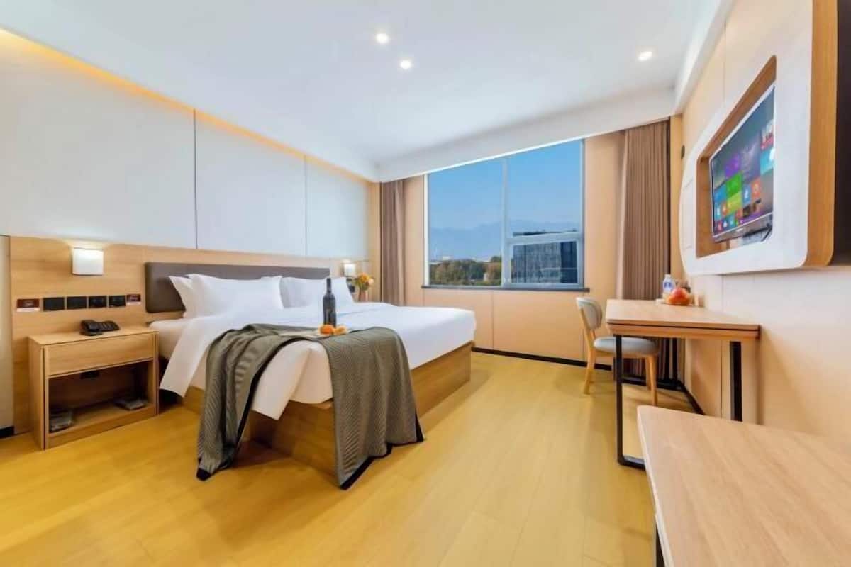 A modern hotel room with a large bed, a desk, a chair, and a TV mounted on the wall.
