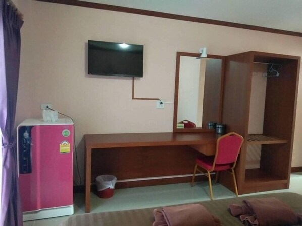 A hotel room with a wooden desk, a red chair, a television mounted on the wall, a wardrobe, and a pink minibar.