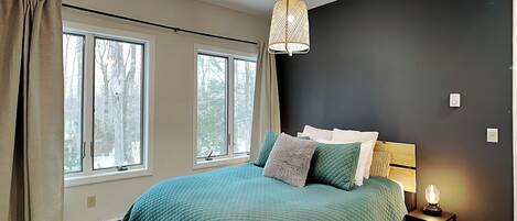 A bedroom with a large bed, two windows, a black accent wall, and a bedside lamp.