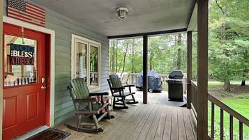 A covered porch with rocking chairs, a grill, and a door with a patriotic sign.