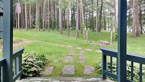 A covered outdoor area with a stone pathway leading through a grassy field surrounded by tall trees.