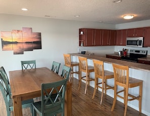 A kitchen with wooden cabinets, a wooden dining table with chairs, and a painting on the wall.