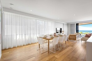 A modern living room with a dining area, wooden flooring, white furniture, and a large window with a view.