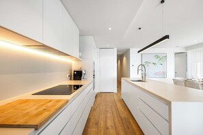 A modern kitchen with white cabinetry, a wooden countertop, and a built-in espresso machine.