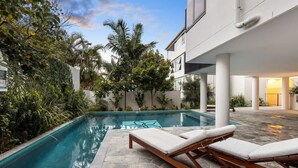 Una piscina con sillas de descanso, rodeada de vegetación y arquitectura moderna.