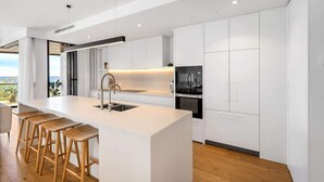 Una cocina moderna con una isla central, taburetes de bar y armarios blancos.