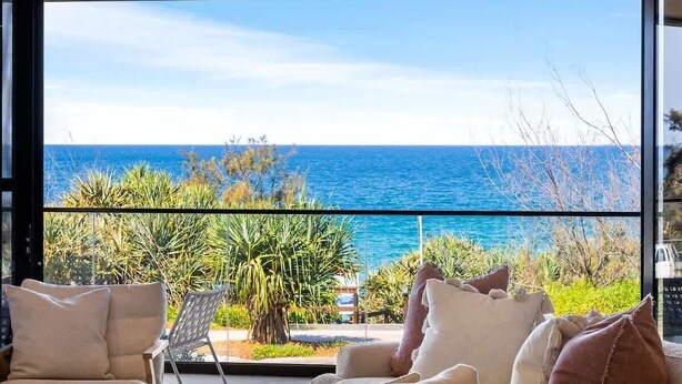 Una habitación con una ventana grande que da a vistas de la costa, una silla y una mesita.