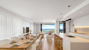 Una cocina moderna con una isla grande, comedor con vistas y sala de estar con sofá y televisor.