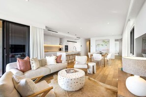 A modern living room with a sofa, ottoman, and chairs, a dining area with a table and chairs, and a kitchen in the background. - Coolum First Bay 121 131 (Coolum Beach)