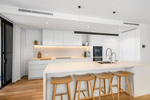 A modern kitchen with white cabinetry, a central island with stools, and a built-in oven.