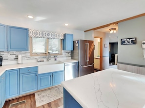 A modern kitchen with blue cabinets, a stainless steel refrigerator, and a white marble countertop. - At Lake's Edge by Taylor Made Deep Creek (McHenry)