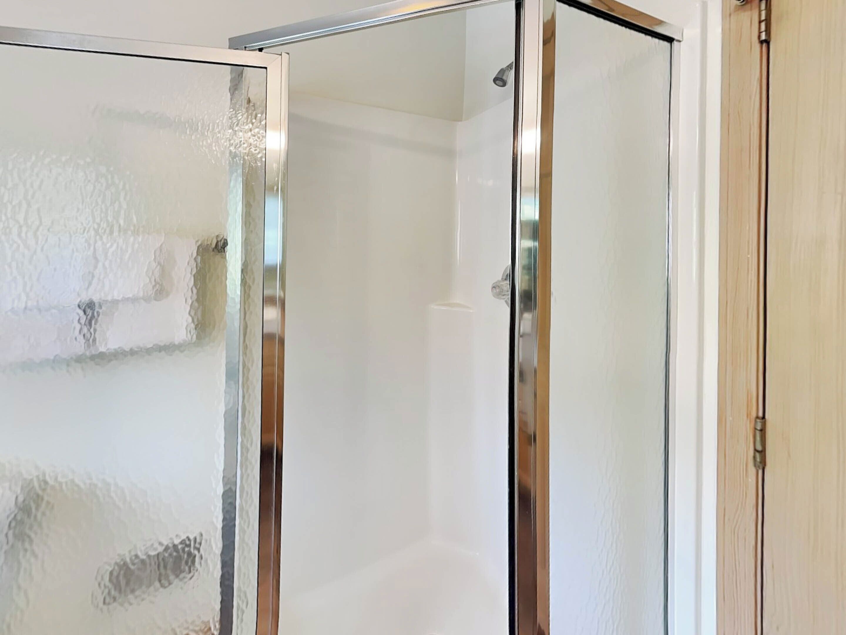 A glass-enclosed shower area with a white tiled wall and a wooden door frame.