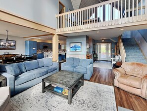 A spacious living area with a high ceiling, a balcony, and a kitchen in the background. - At Lake's Edge by Taylor Made Deep Creek (McHenry)