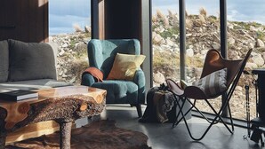 Un interior moderno con un ventanal grande, un sillón azul, una butaca de cuero y una mesa de madera rústica.