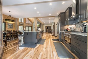 A spacious kitchen with wooden flooring, modern appliances, and a dining area with wooden furniture. - Away in the Mountains by Taylor Made Deep Creek (McHenry)