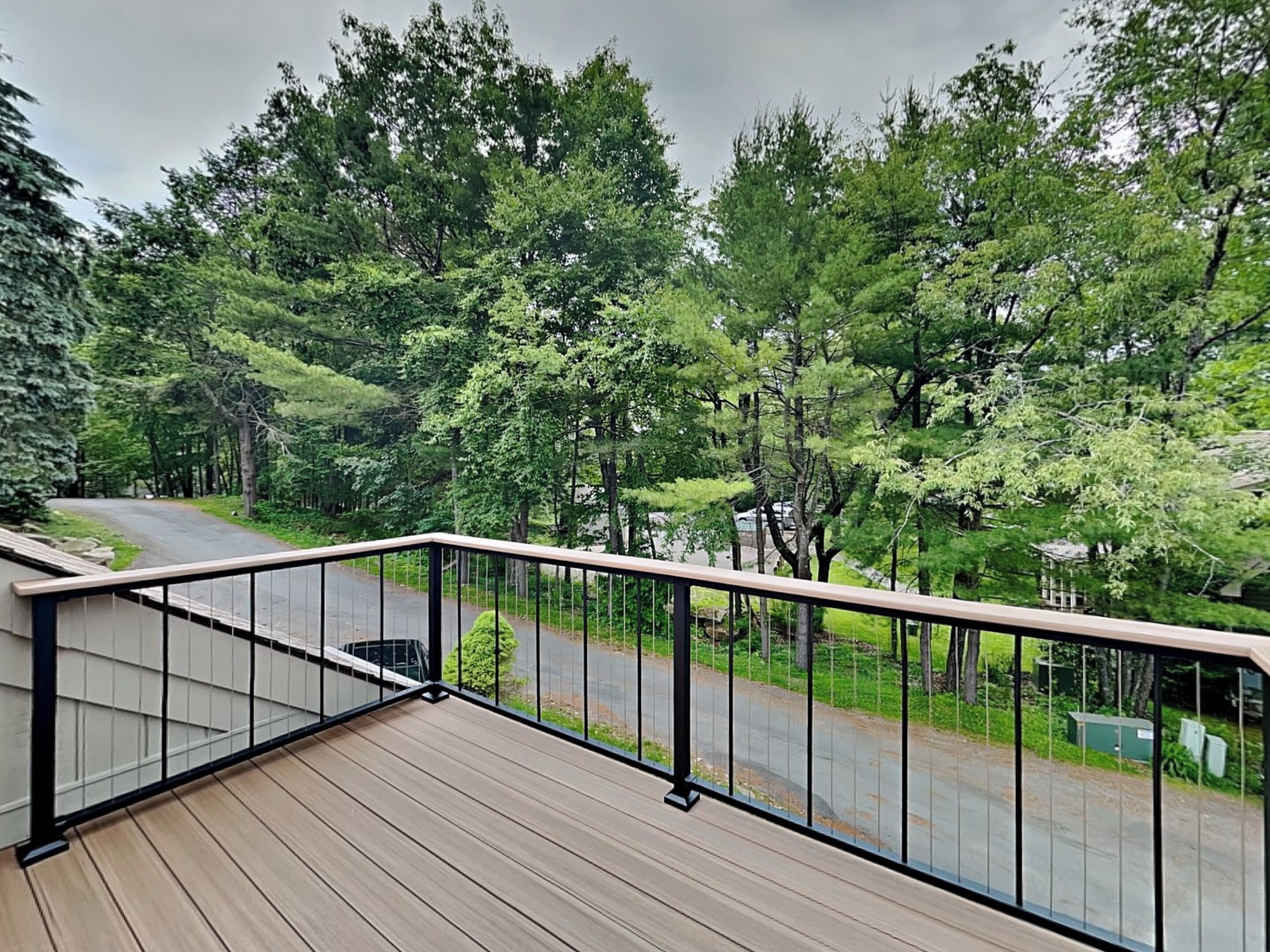 A wooden deck with a metal railing overlooking a road and dense greenery.