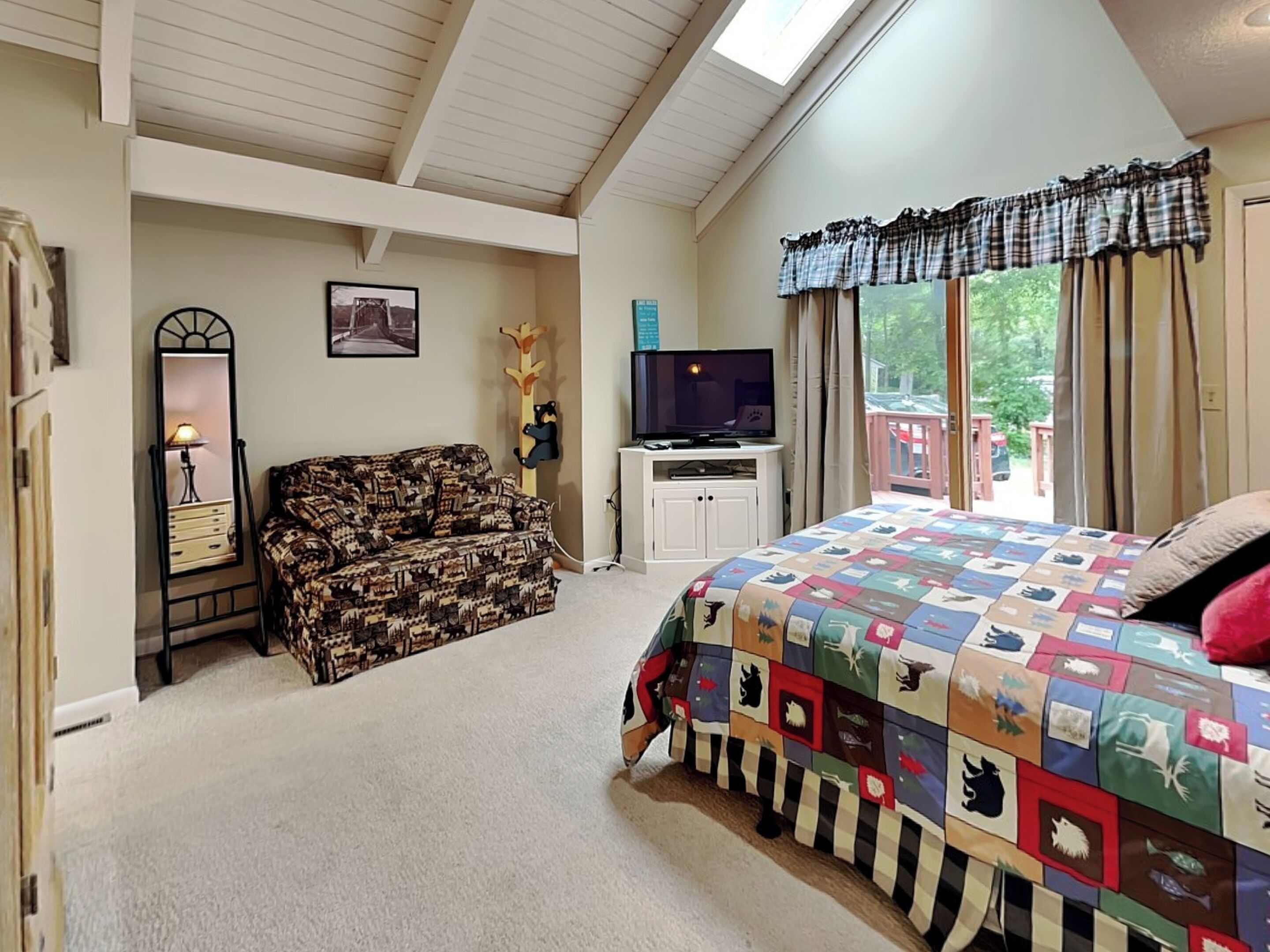 A bedroom with a large bed, a sofa, a TV, and a window with curtains.