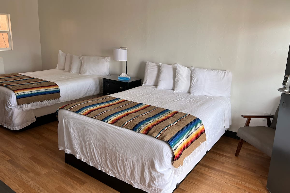 A hotel room with two beds, a nightstand with a lamp, and a chair.