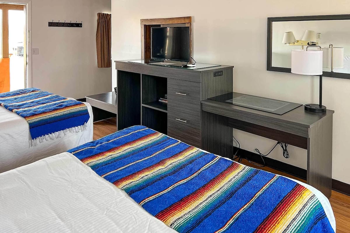 A hotel room with two beds, a desk, a television, and a mirror.