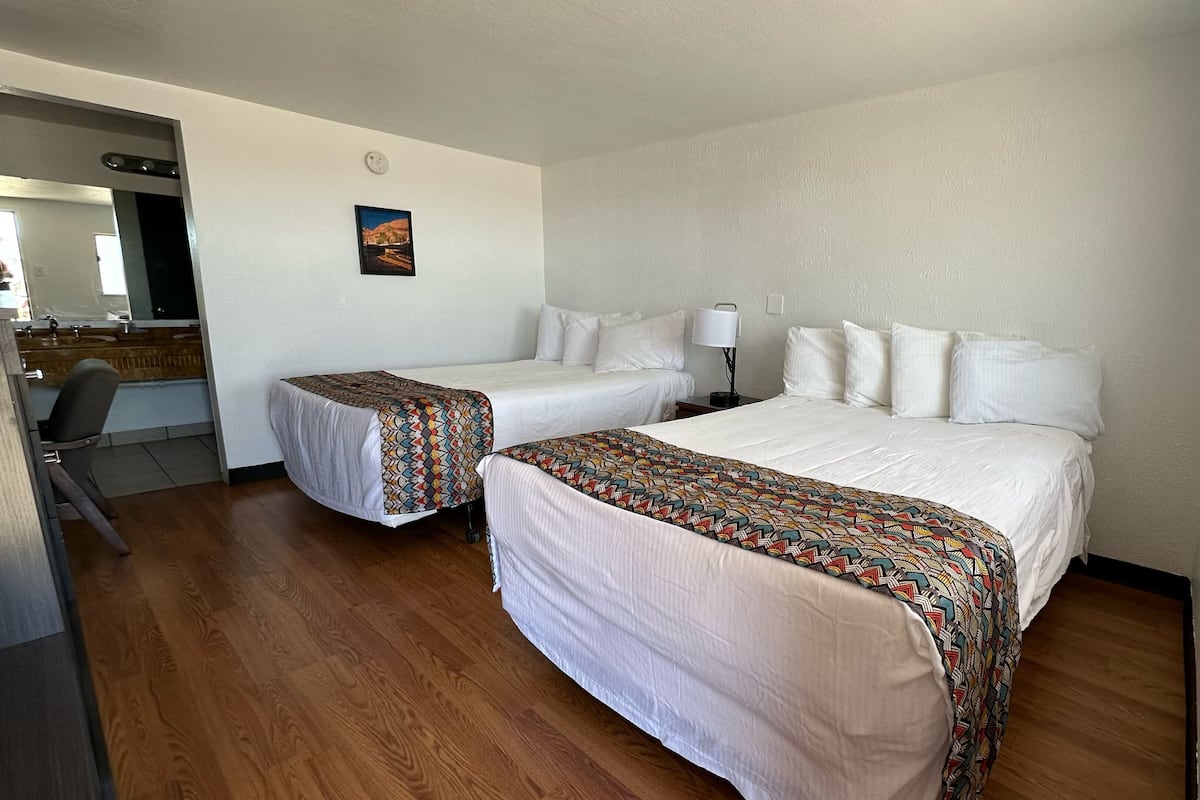 A hotel room with two beds, a desk, a chair, a bathroom, and a window.