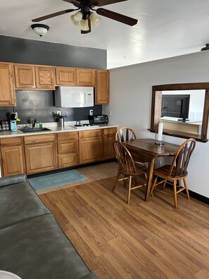 A modern kitchen with wooden cabinets, a microwave, and a dining area with a table and chairs. - Escalante Canyon Inn (Escalante)
