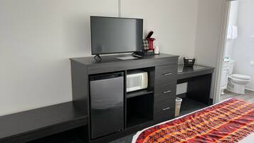 A hotel room with a dark wooden desk, a flat-screen TV, a microwave, and a small refrigerator.