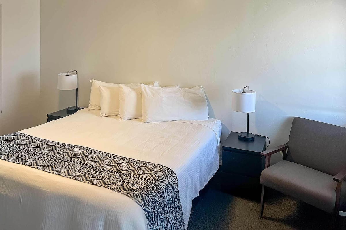 A hotel room with a bed, two bedside tables, a chair, and a lamp.