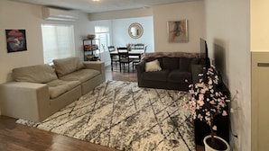 A living room with a sofa, a coffee table, and a dining area with a table and chairs. - Family Gathering Place 6 BD Home Hot Tub sleeps 12 (American Fork)