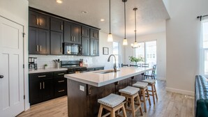 A modern kitchen with dark cabinets, a large island with stools, and pendant lighting. - Family Gathering Place 6 BD Home Hot Tub sleeps 12 (American Fork)