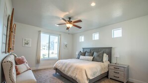 A bedroom with a bed, a nightstand, a chair, a ceiling fan, and a window. - Family Gathering Place 6 BD Home Hot Tub sleeps 12 (American Fork)