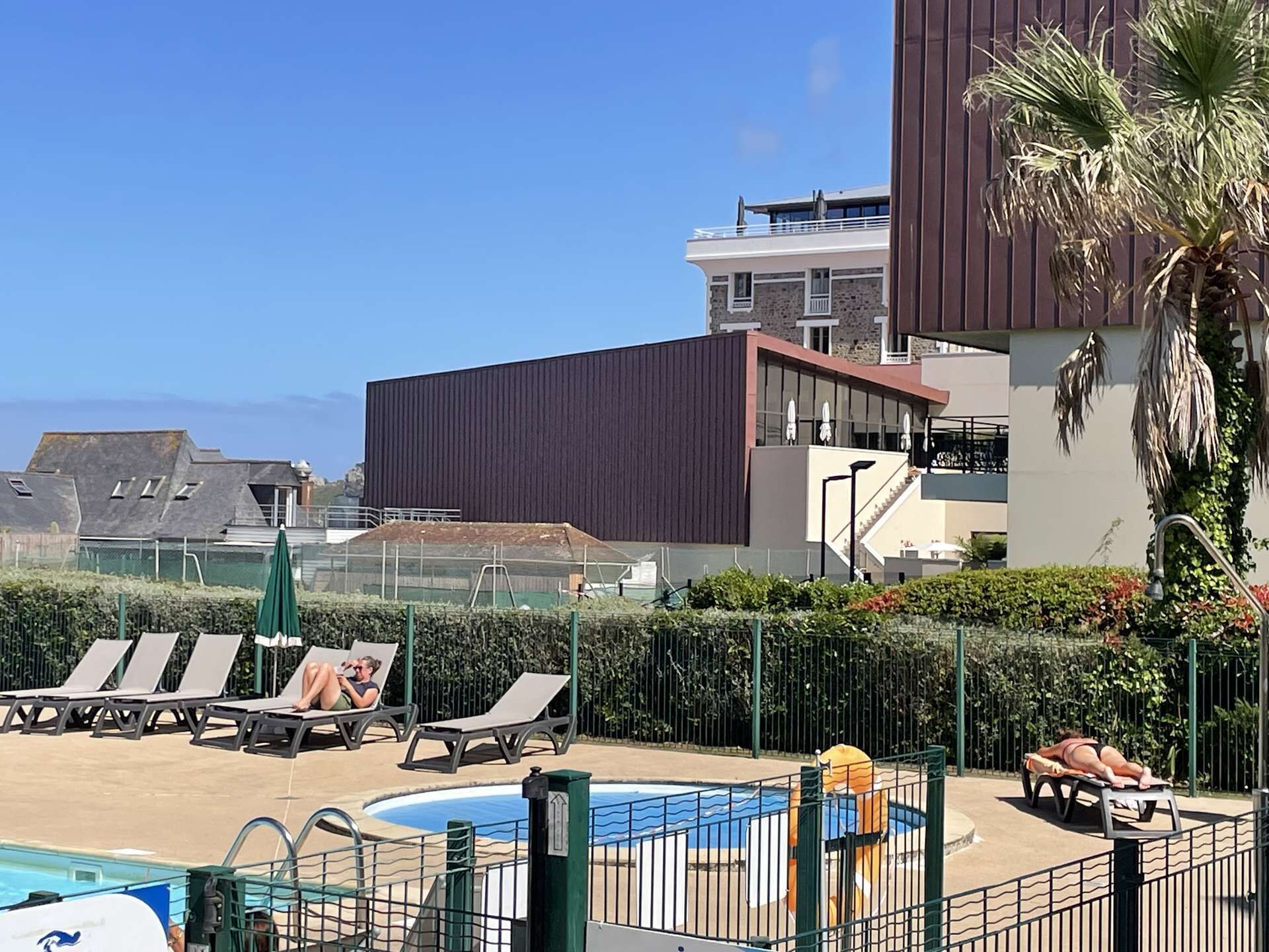 Uma área de piscina com espreguiçadeiras, uma piscina e um edifício moderno com varandas.
