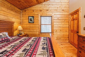 Un dormitorio de cabaña de madera con una cama, una mesita de noche, una ventana y un armario.