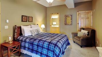A bedroom with a bed, a chair, a nightstand, a ceiling fan, a mirror, and a door.