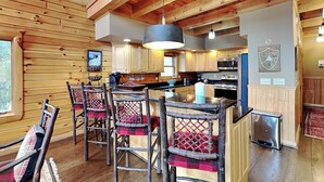 A rustic cabin interior with a wooden interior, a kitchen area, and a dining space with bar stools. - Bear Hollow Lodge by Taylor Made Deep Creek (Oakland)