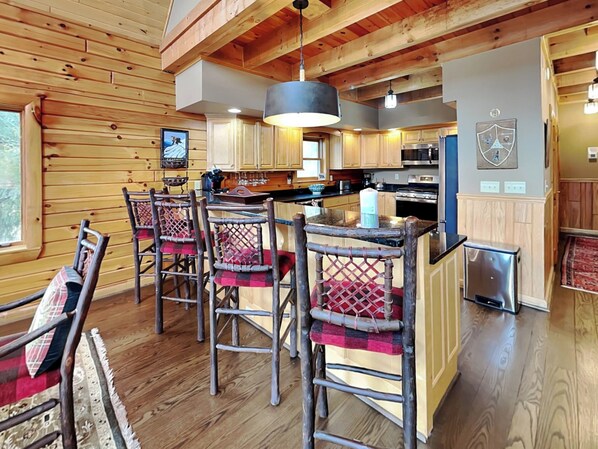 A rustic cabin interior with a wooden interior, a kitchen area, and a dining space with bar stools.