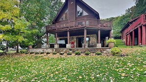 A two-story wooden house with a balcony, surrounded by trees and a grassy area. - Bear Hollow Lodge by Taylor Made Deep Creek (Oakland)