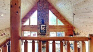 A wooden interior with a stone fireplace, wooden beams, and a view of the outdoors. - Bear Hollow Lodge by Taylor Made Deep Creek (Oakland)