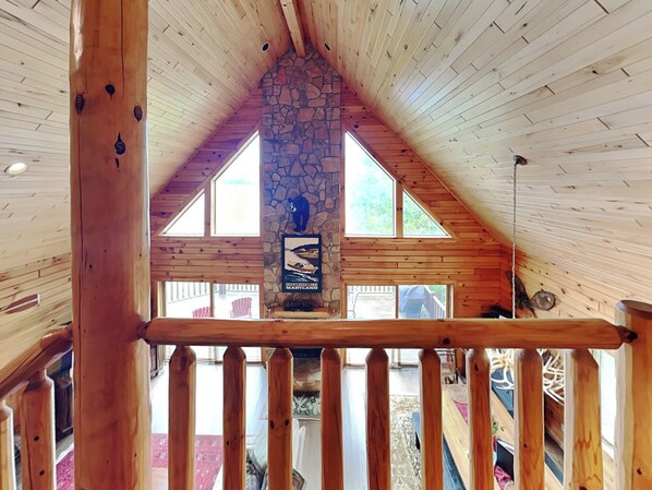 A wooden interior with a stone fireplace, wooden beams, and a view of the outdoors.