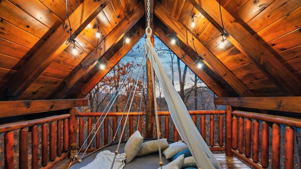 Une terrasse en bois avec un hamac et des coussins, une balustrade en bois et une vue sur les arbres.
