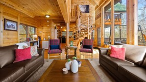 L’intérieur d’un chalet confortable, avec des murs en bois, un canapé en cuir marron, des fauteuils à carreaux et un escalier en bois.