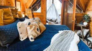 Une chambre confortable avec un grand lit, un fauteuil suspendu et une vue sur l’extérieur.