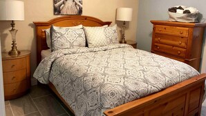 Une chambre à coucher avec un lit en bois, deux tables de chevet avec des lampes, une commode en bois et un tableau au mur.