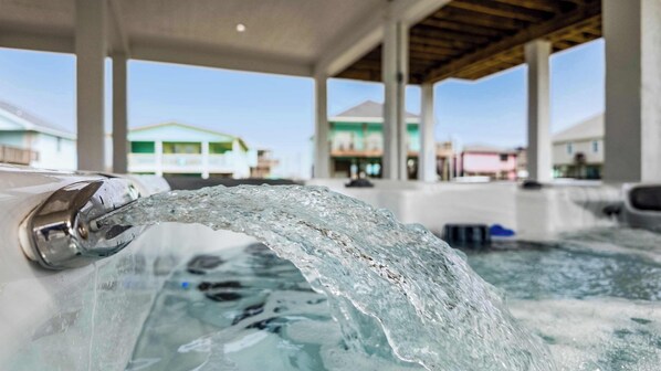 A hot tub with water flowing from a spout, surrounded by a covered area with a view of buildings in the background.