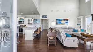 Un vaste salon doté d’un grand canapé d’angle, d’un coin repas avec des chaises en osier et d’une cuisine à l’arrière-plan.