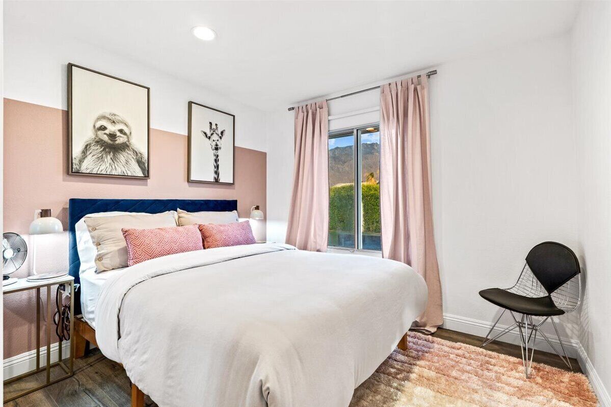 A bedroom with a bed, a chair, a fan, and two wall-mounted artworks.