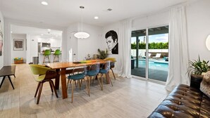 Una sala de estar moderna con comedor, un ventanal con vista a una piscina y un mural en la pared.