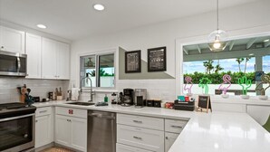 Una cocina moderna con armarios blancos, electrodomésticos de acero inoxidable y un amplio ventanal con vistas al verdor.