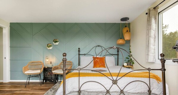 A bedroom with a bed, two wicker chairs, a small table, and a window with curtains.
