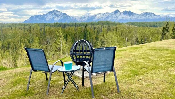 Un área de descanso con dos sillas y una mesa, con vista a un bosque y montañas.
