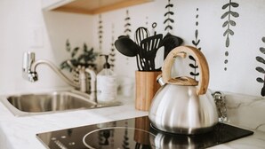 Una cocina moderna con un hervidor de acero inoxidable sobre una cocina de inducción, un fregadero y un portalápices de madera.